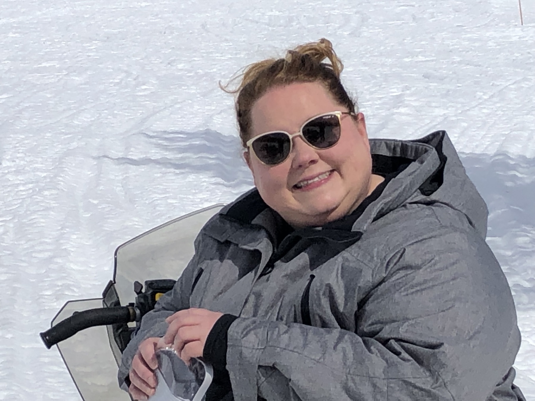 Amy out on a snowmobile in the snow, sunglasses on.